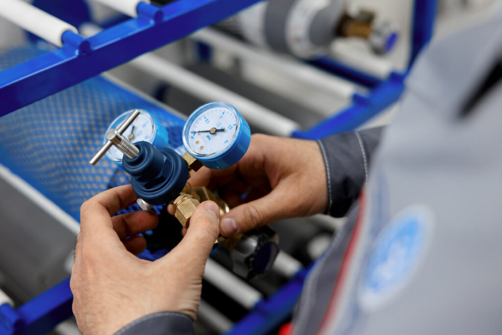 A metrology laboratory specialist takes a compressed gas cylinder for testing and verification. The man connects the pressure gauge. Analyze gas and check connections for leaks.
