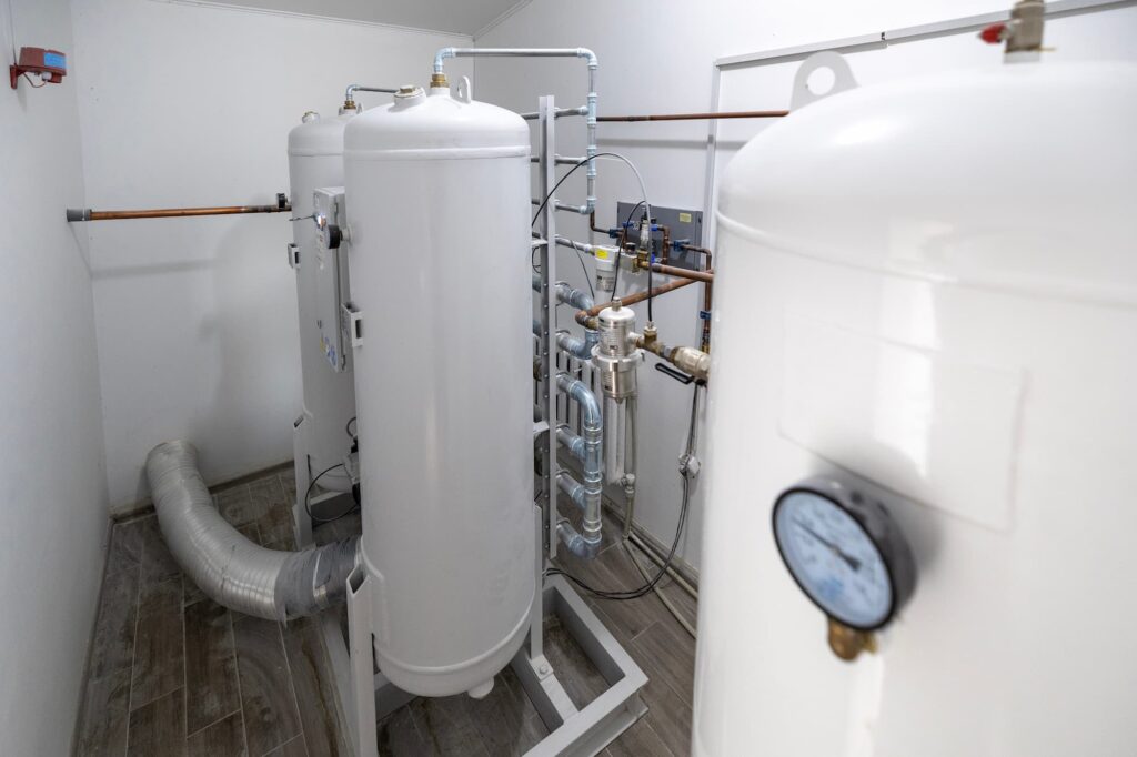 A modern oxygen generation plant, with large white tanks, pipes, and gauges, supplies medical-grade oxygen to healthcare facilities. It stands in a sterile utility room.